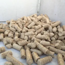 Jasne, cylindryczne brykiety pelletu drzewnego, ułożone w pryzmę na białym tle, widoczne drobne pęknięcia na powierzchni niektórych pelletów.