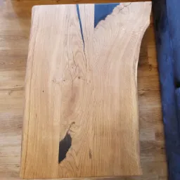 Stolik kawowy z blatem z litego drewna dębowego z żywicą epoksydową w kolorze czarnym, ukazujący naturalne pęknięcia i słoje drewna, z nieregularną krawędzią.