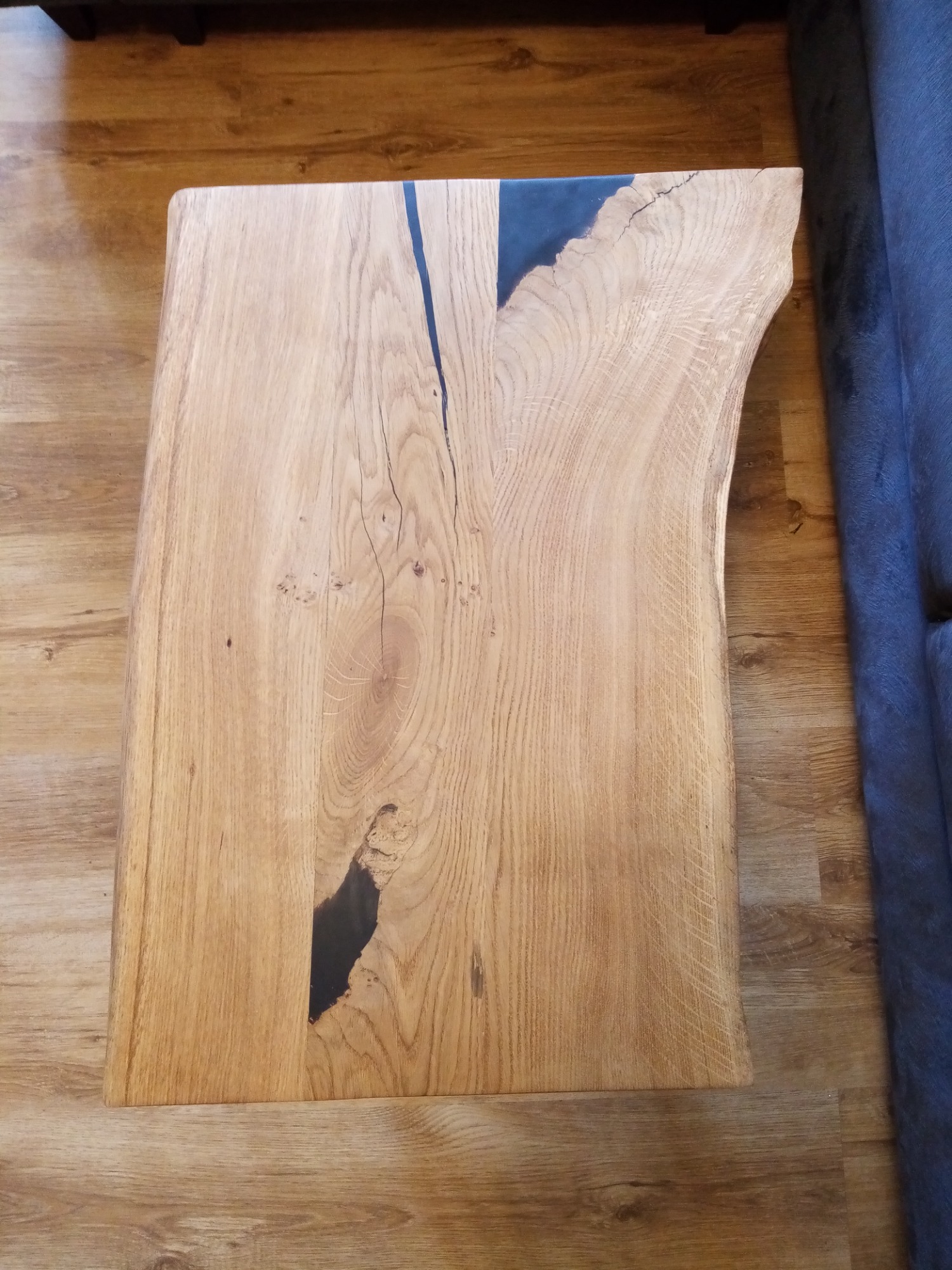 Stolik kawowy z blatem z litego drewna dębowego z żywicą epoksydową w kolorze czarnym, ukazujący naturalne pęknięcia i słoje drewna, z nieregularną krawędzią.