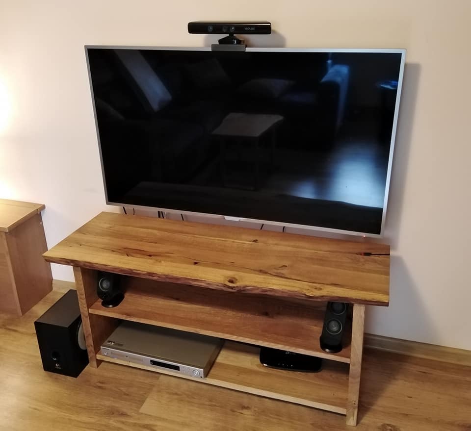 Stolik RTV z drewna o naturalnych krawędziach, z półkami na sprzęt audio i wideo, pod telewizorem z kamerą Kinect.