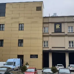 Widok na elewację hotelu Royal Hotel & Spa w Białymstoku z widoczną instalacją klimatyzacyjną na dachu oraz zaparkowanymi samochodami przed budynkiem.