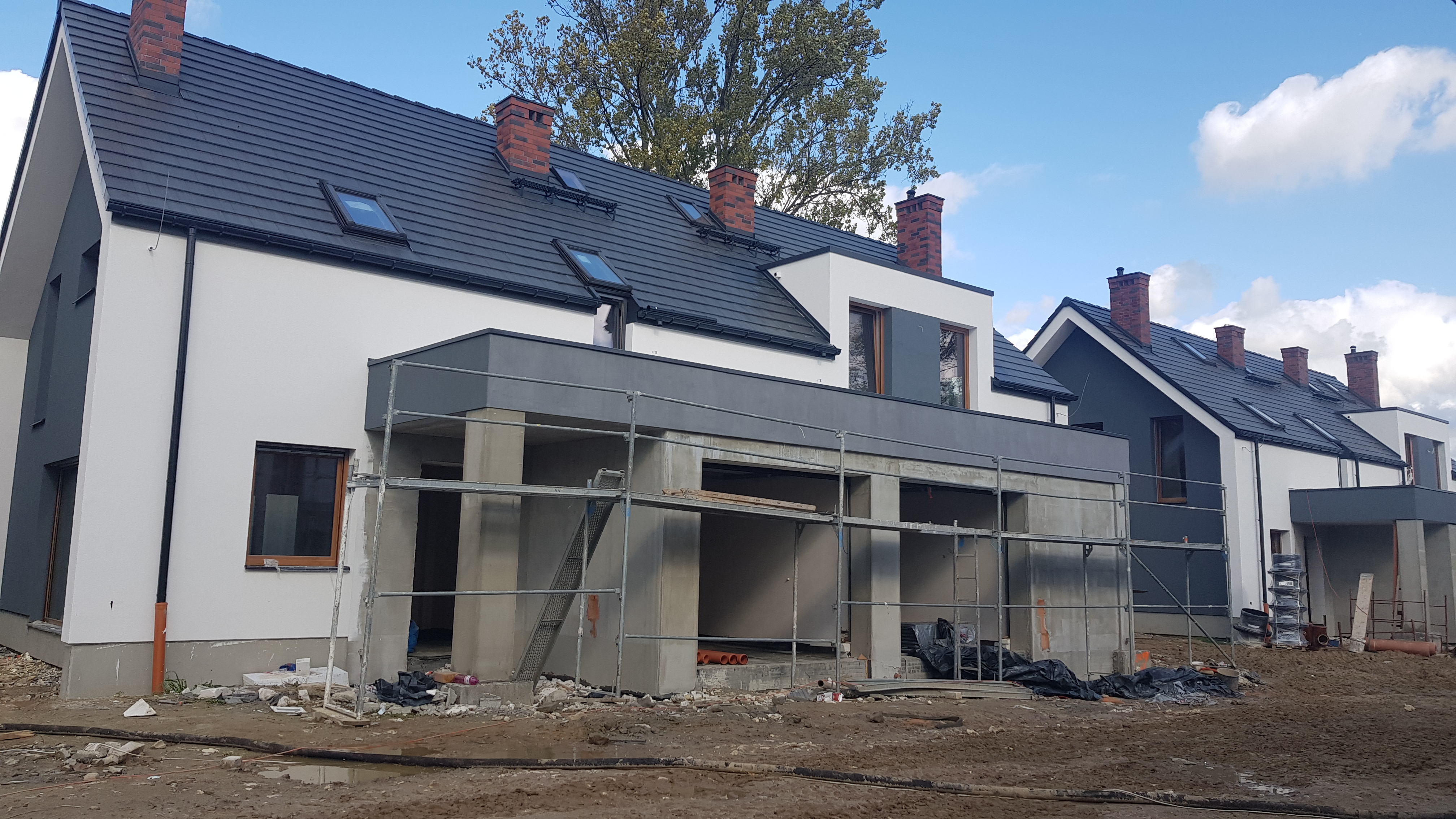 Nowoczesne domy w zabudowie szeregowej w trakcie budowy, widoczne rusztowania i niedokończone elementy elewacji.