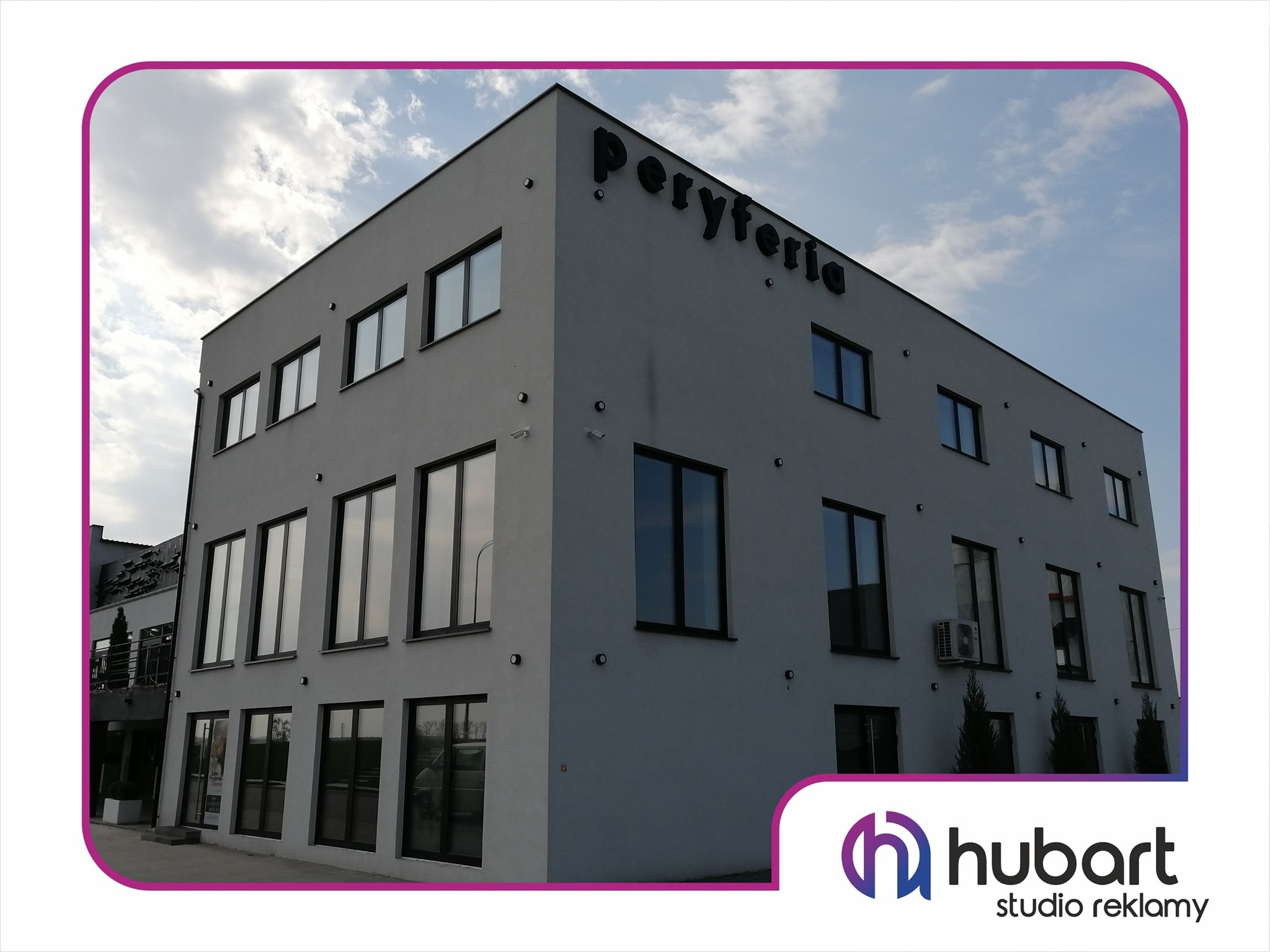 Nowoczesny budynek z ciemnymi oknami, na fasadzie czarny napis 'Peryferia', w prawym dolnym rogu logo 'Hubart studio reklamy'.