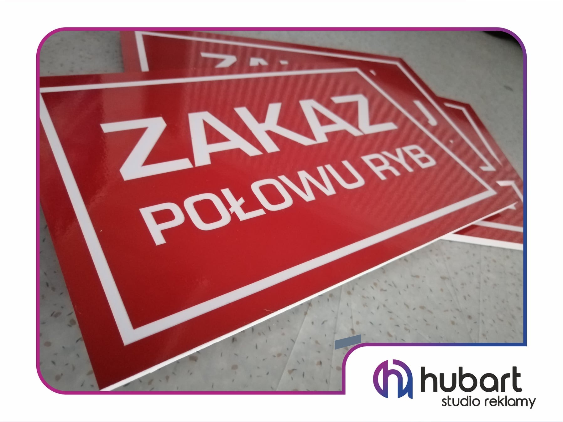 Stos czerwonych tabliczek z białym napisem 'ZAKAZ POŁOWU RYB' w prostokątnej ramce, ułożonych na szarym tle, z logo firmy 'Hubart studio reklamy' w prawym dolnym rogu.