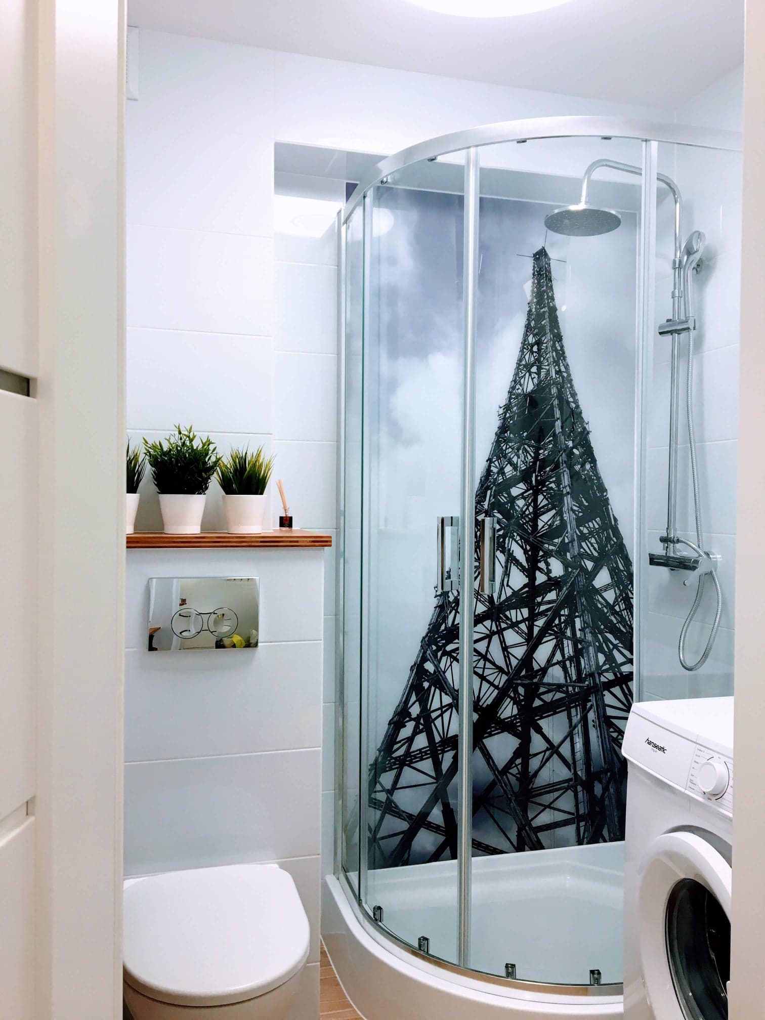 Nowoczesna łazienka z kabiną prysznicową z grafiką wieży Eiffla, białe płytki, pralka Hanseatic i minimalistyczne dekoracje.