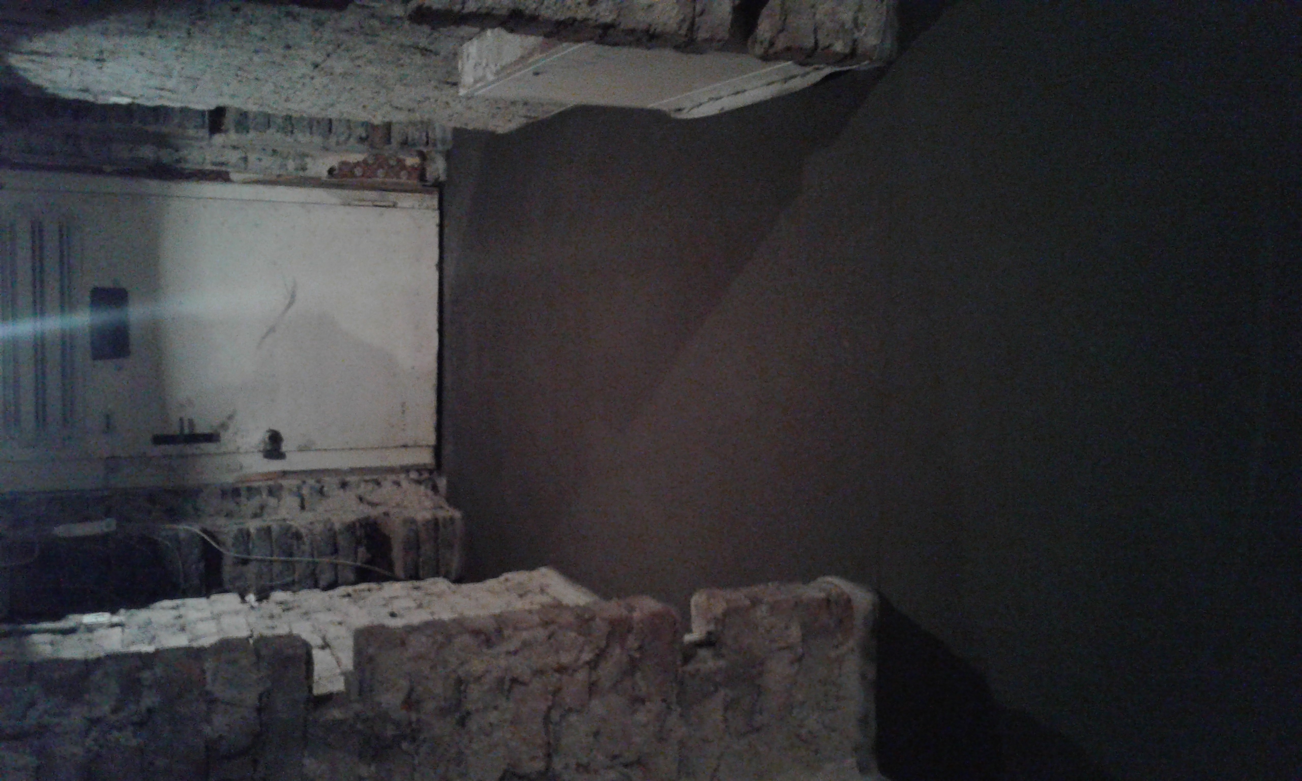 Surowy mur z cegły i fragment ściany po nałożeniu tynku w trakcie remontu. Widoczne ślady po instalacjach elektrycznych i hydraulicznych.