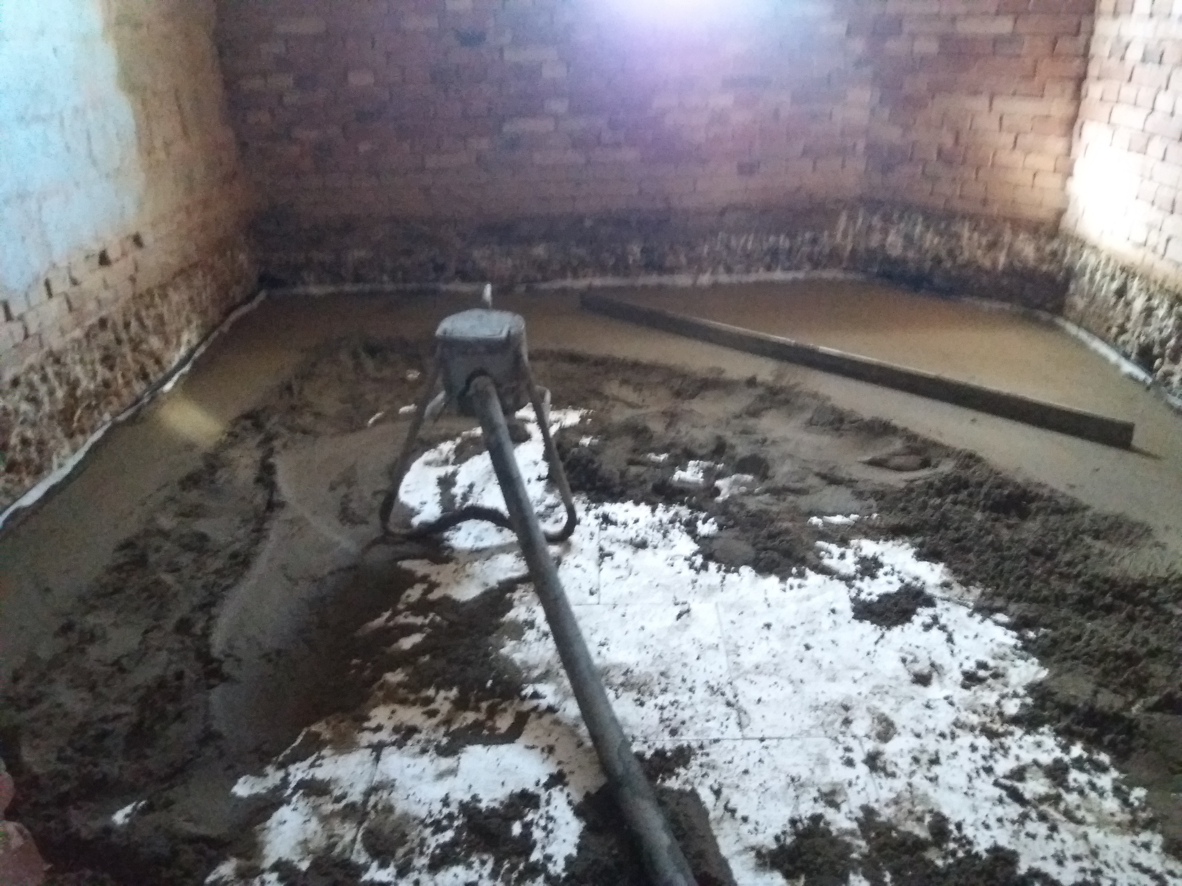 Wylewka posadzki w trakcie wykonywania, widoczne narzędzia i surowa cegła na ścianach.