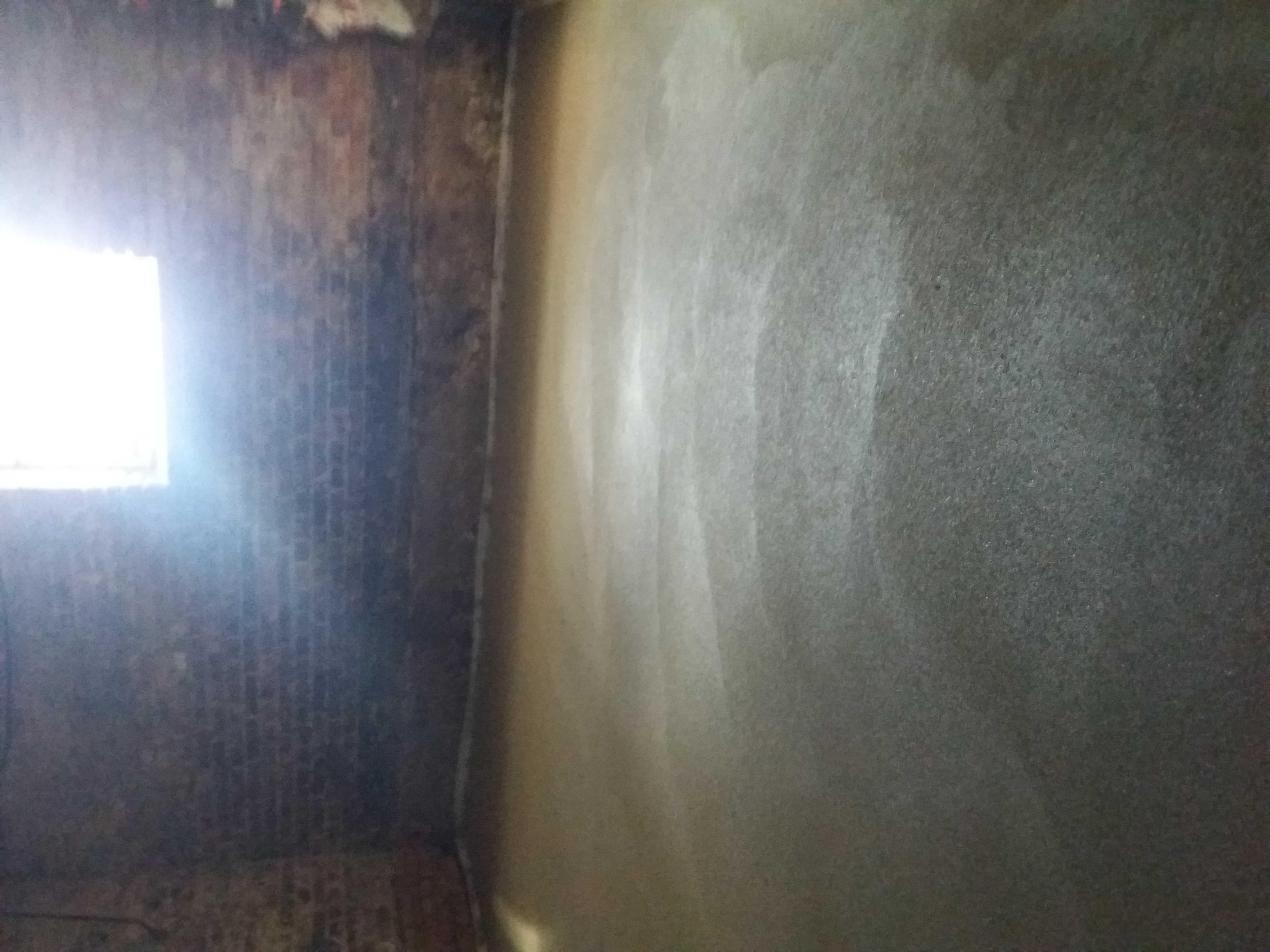 Surowa ściana z cegły z oknem obok gładkiej, świeżo nałożonej zaprawy cementowej na ścianie w pomieszczeniu w trakcie remontu.