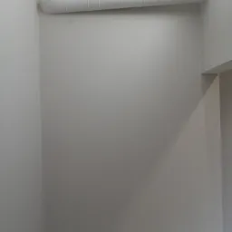 Pomieszczenie po świeżym malowaniu na szaro, widoczny przewód wentylacyjny pod sufitem i ślady po niedoskonałościach przed malowaniem.