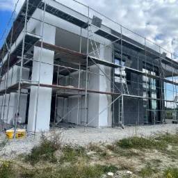 Ocieplanie elewacji budynku we Wrocławiu z użyciem rusztowania, widoczne fragmenty ocieplenia i pracownik przy wiadrach z materiałem.