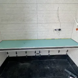 Wnętrze łazienki w trakcie remontu: ułożone płytki podłogowe w czarnym kolorze, częściowo wykończone ściany jasnymi płytkami, widoczne uchwyty do mocowania płyt karton-gips na suficie, wystające...