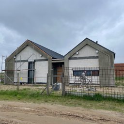 AGARPBUD Sp. z o.o. - Surowy stan budynku jednorodzinnego w trakcie prac wykończeniowych elewacji, widoczne rusztowania, ocieplenie oraz pracownicy w kombinezonach ochronnych. Budynek z białego bloczka, z ciemnym dachem...