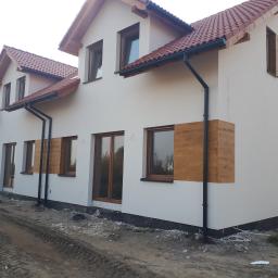 AGARPBUD Sp. z o.o. - Nowo wybudowane segmenty mieszkalne z ocieploną elewacją, z widocznymi fragmentami imitacji drewnianej okładziny wokół okien, orynnowaniem i przygotowanym terenem wokół budynków.