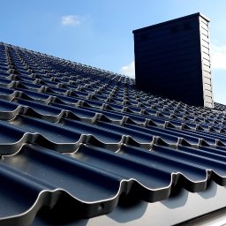 Firma ogólnobudowlana 'Deker' - Nowy, czarny dach z dachówki modułowej, z widocznym kominem i rynną. Ujęcie z dołu, podkreślające regularność wzoru i estetykę wykonania. Błękitne niebo w tle.