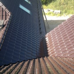 Firma ogólnobudowlana 'Deker' - Nowy, brązowy dach z dachówki ceramicznej, z widocznym kominem i oknami dachowymi. Na drugim planie zielona trawa i czerwony samochód dostawczy.