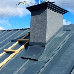 Firma ogólnobudowlana 'Deker' - Szary dach z blachy trapezowej z kominem i drewnianą konstrukcją, widok z góry, błękitne niebo w tle. Detal pokrycia dachowego w trakcie montażu.