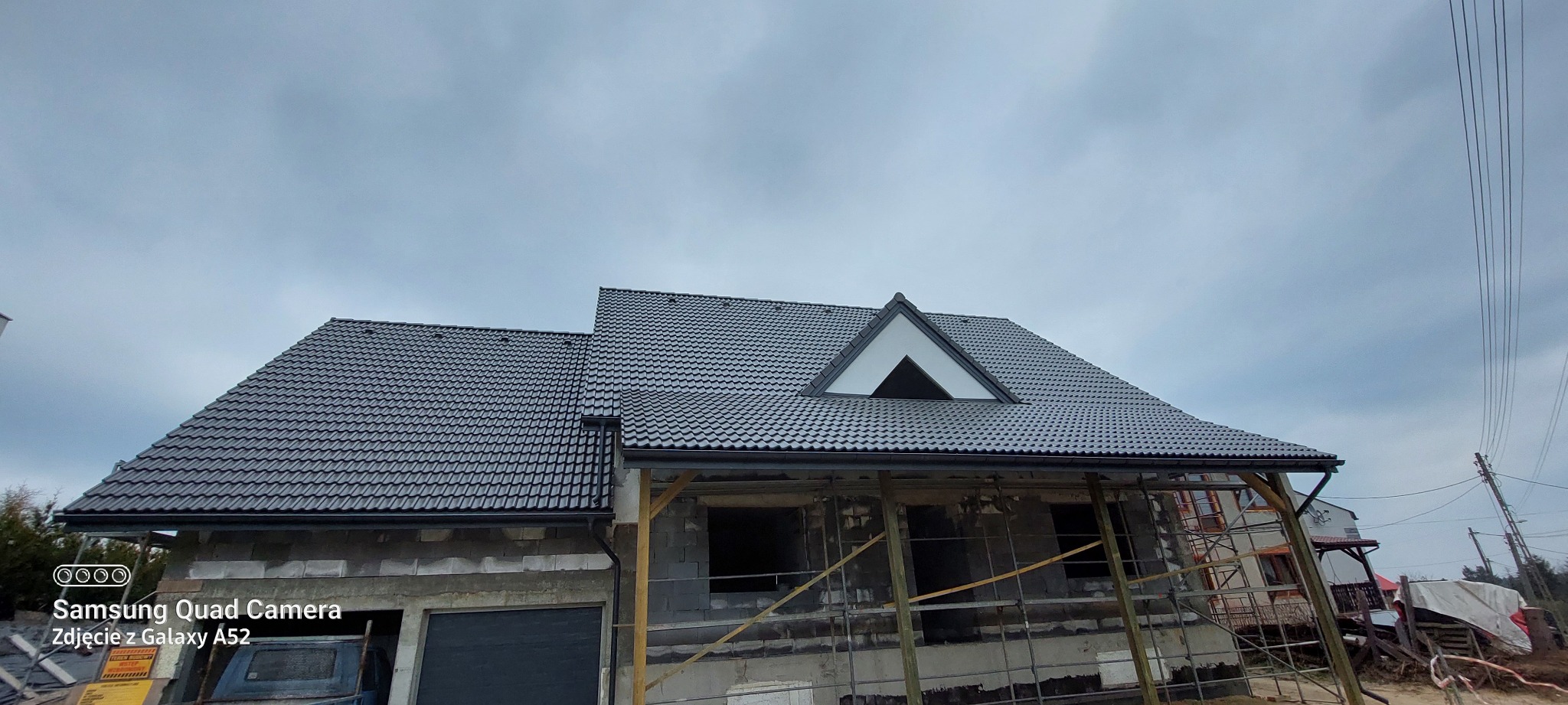 Nowy dach z czarnej dachówki karpiówki na domu w stanie surowym otwartym w Nowej Brzeźnicy. Widoczne obróbki blacharskie i rynny.