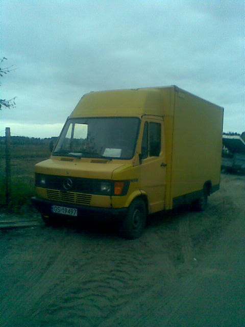 Żółty samochód dostawczy Mercedes z numerem rejestracyjnym GS 19497, zaparkowany na piaszczystym terenie, sugerujący transport materiałów instalacyjnych lub narzędzi hydraulicznych.