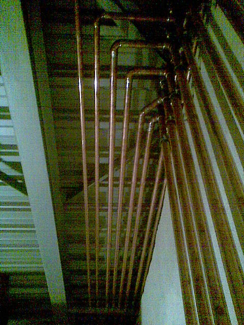 Miedziane rury instalacji grzewczej, zamontowane pod sufitem, z widocznymi złączkami i kolankami, w słabym oświetleniu.