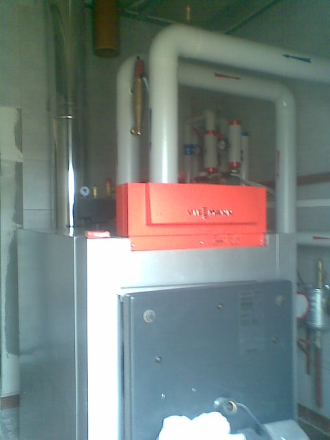 Nowoczesny piec grzewczy Viessmann z widocznymi rurami instalacji CO w surowym pomieszczeniu.