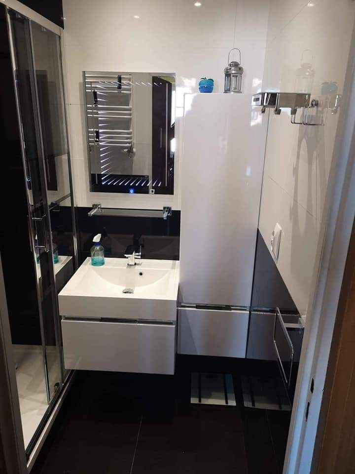 Nowoczesna łazienka z czarno-białymi płytkami, umywalką nablatową, podświetlanym lustrem i kabiną prysznicową ze szklanymi drzwiami.