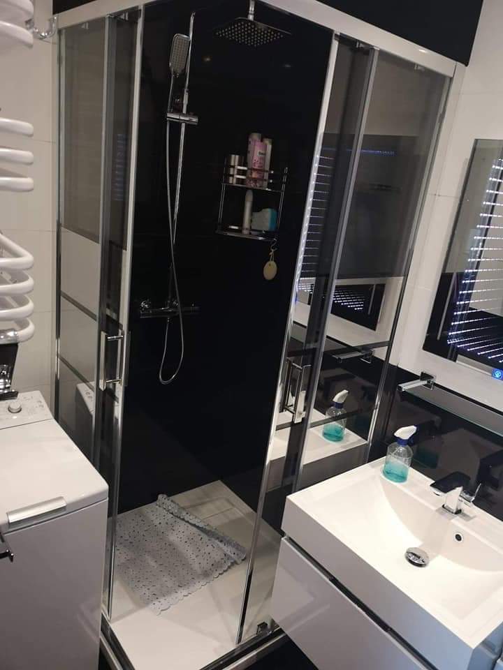 Nowoczesna łazienka z czarnymi ścianami w kabinie prysznicowej, białą umywalką z szafką i grzejnikiem drabinkowym, widoczna mata antypoślizgowa w brodziku.