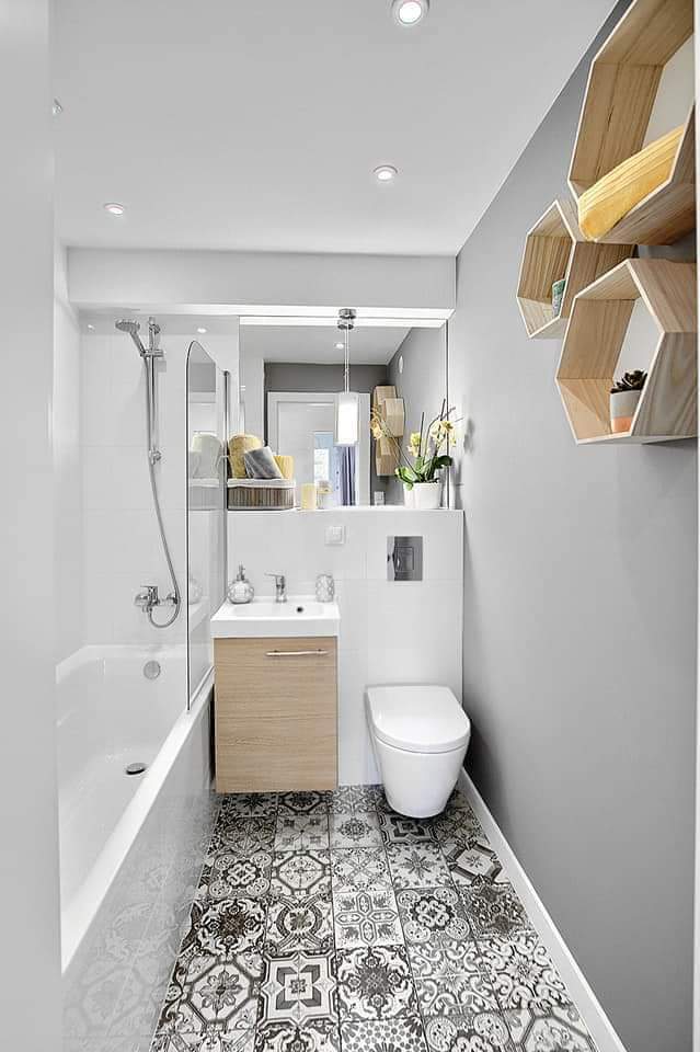 Nowoczesna łazienka w odcieniach bieli i szarości z wzorzystą podłogą, drewnianą szafką pod umywalką i heksagonalnymi półkami na ścianie.