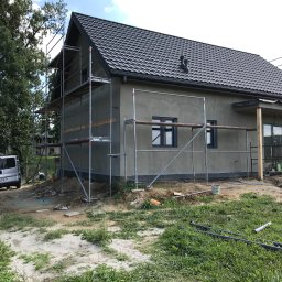 Domy szkieletowe MK - Dom jednorodzinny w trakcie prac wykończeniowych elewacji, otoczony rusztowaniami, widoczny samochód dostawczy w tle.