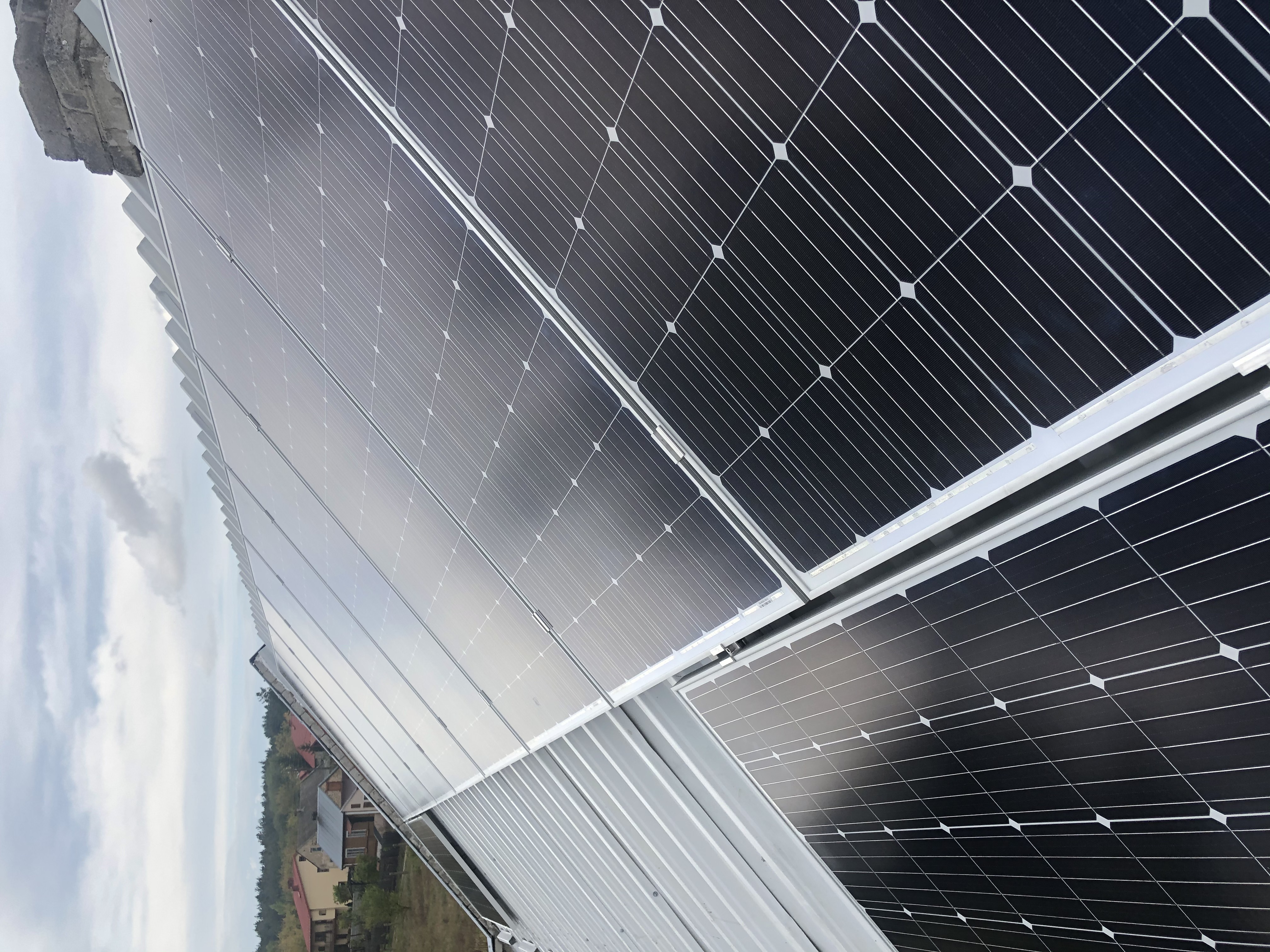 Panel słoneczny zamontowany na dachu z widokiem na okoliczne domy i niebo z chmurami.