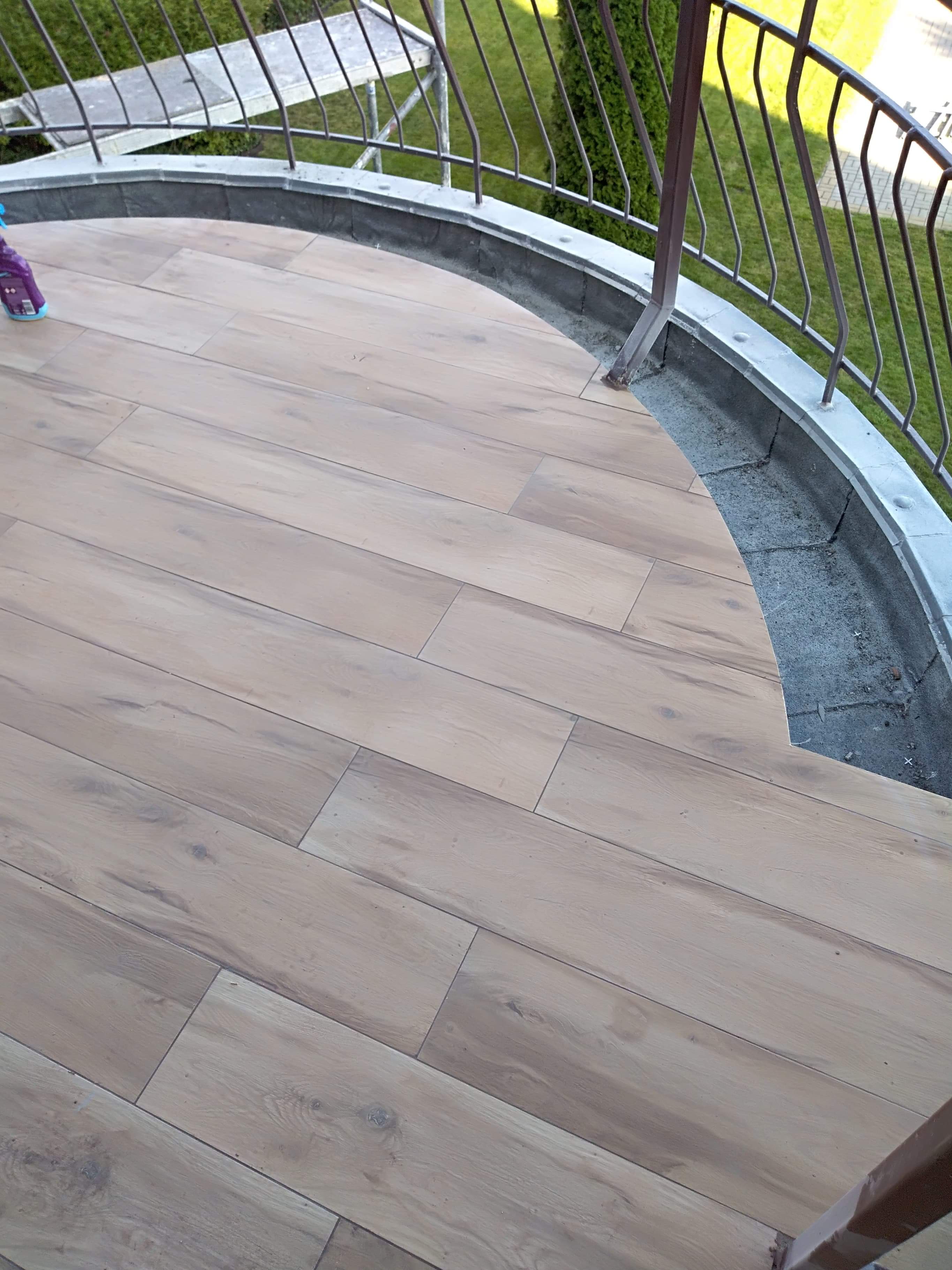 Ułożona podłoga z płytek imitujących drewno na balkonie z metalową balustradą, widoczne niedoróbki przy krawędzi balkonu.