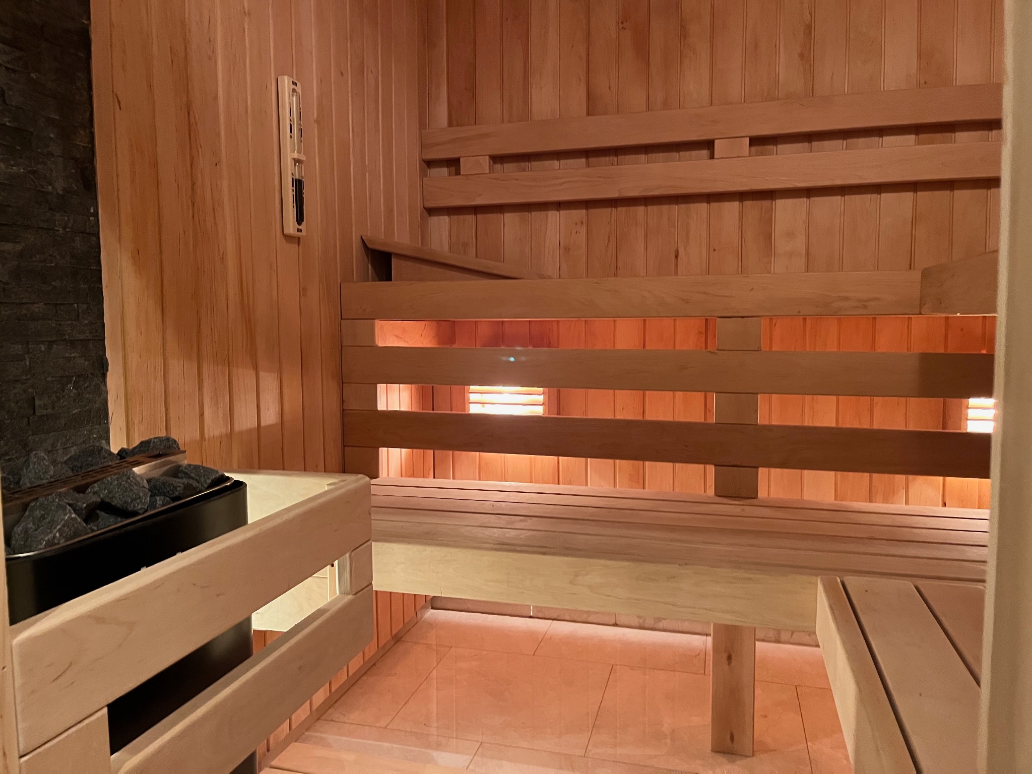Wnętrze drewnianej sauny w Warszawie z kamieniami w piecu, termometrem na ścianie i oświetleniem pod ławkami.