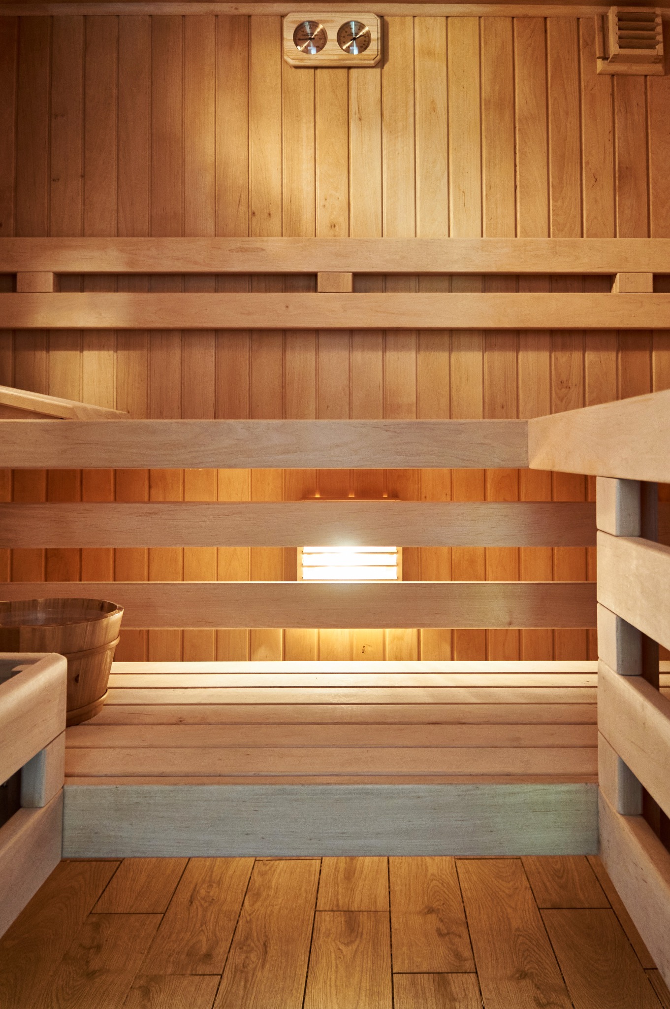 Wnętrze drewnianej kabiny z ławkami, oświetleniem i termometrem/higrometrem na ścianie, widok z dołu na drewnianą podłogę.