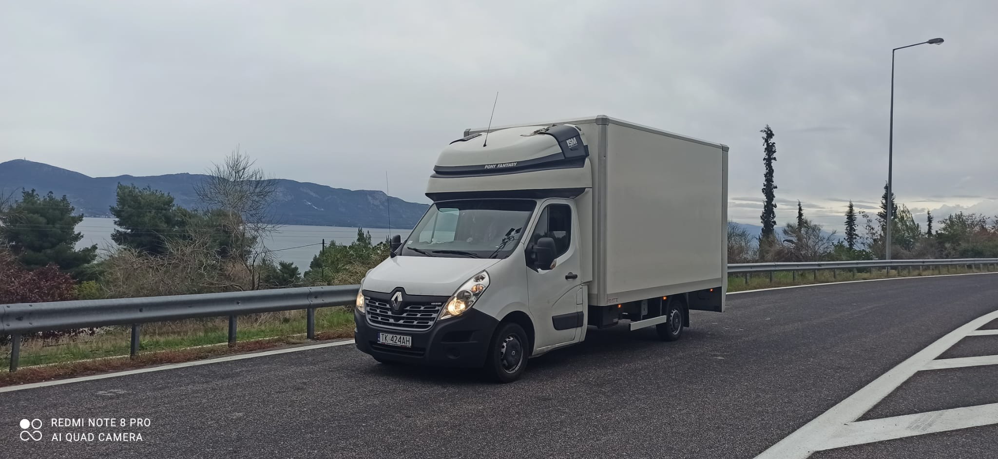 Biały samochód dostawczy Renault Master z zabudową kontenerową Pony Fantasy, zaparkowany na asfalcie z widokiem na góry i jezioro w tle.