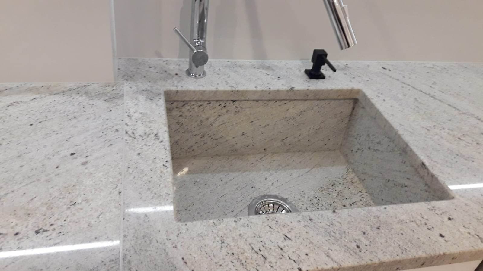 Jasny blat kuchenny z wbudowanym kwadratowym zlewem, bateria i dozownik na płyn do naczyń, widoczny odpływ.