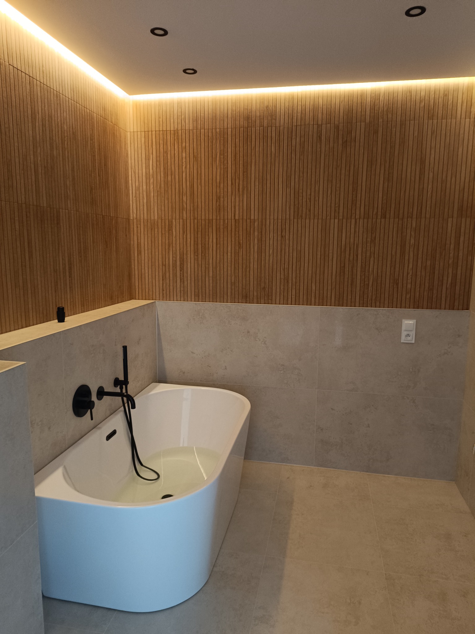 Nowoczesna łazienka z drewnianą boazerią, podświetleniem LED, białą wanną wypełnioną wodą i czarną armaturą.