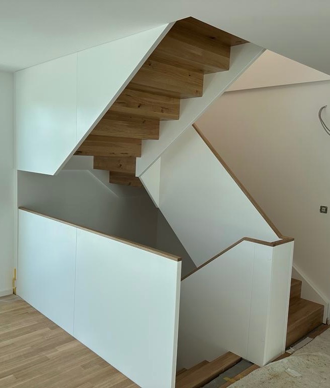 Nowoczesne schody z drewnianymi stopniami i białymi panelami, minimalistyczny design, widoczne wykończenia z jasnego drewna.