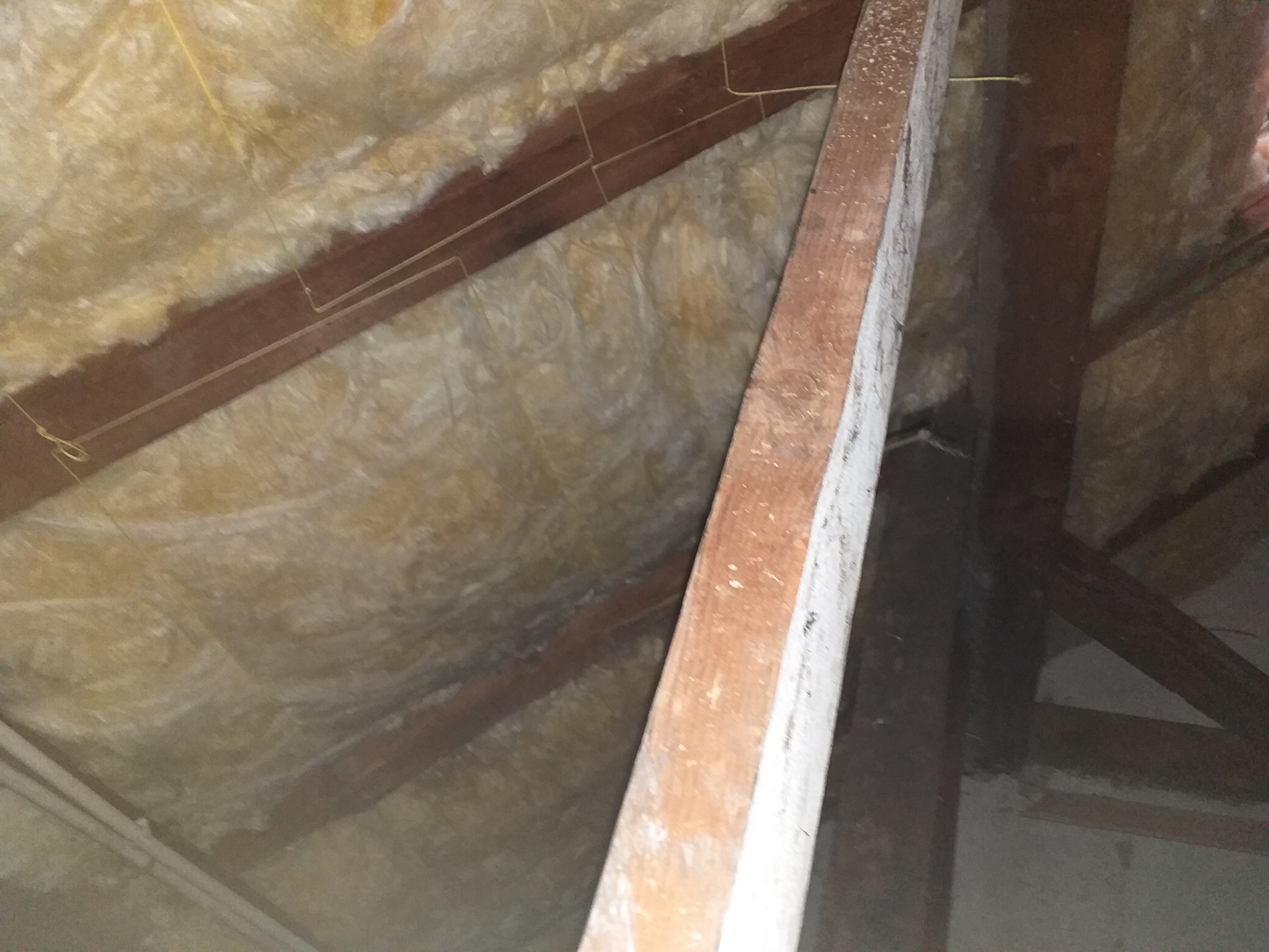 Izolacja poddasza wełną mineralną widoczna między drewnianymi krokwiami, z widocznymi fragmentami przewodów elektrycznych