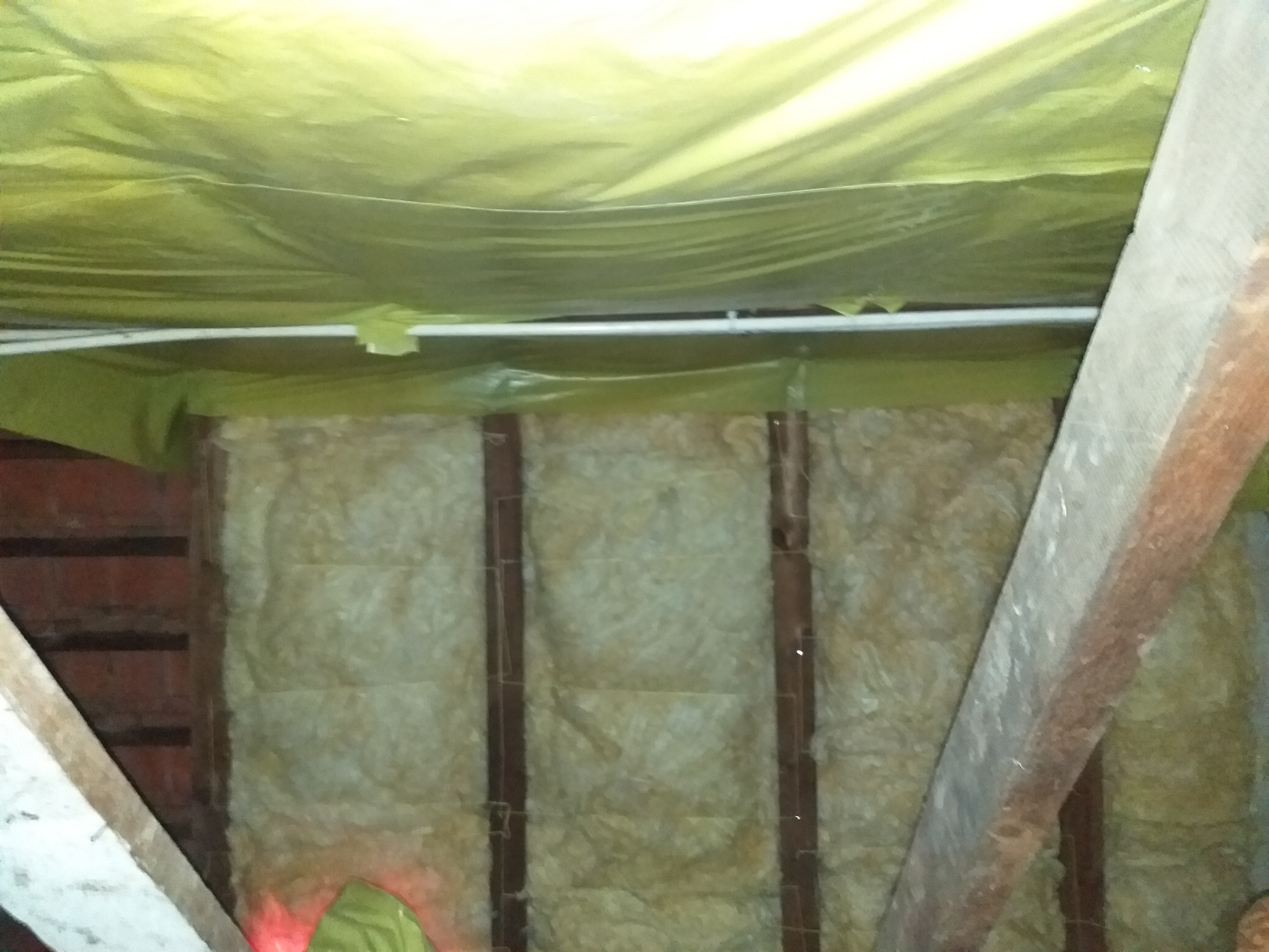 Izolacja poddasza z wełny mineralnej, zabezpieczona folią paroizolacyjną, widoczne drewniane elementy konstrukcyjne dachu.