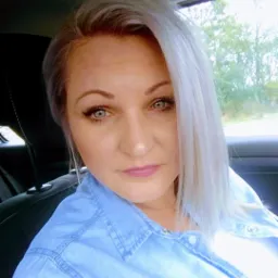 Portret kobiety z platynowymi włosami i niebieską koszulą dżinsową, siedzącej w samochodzie.