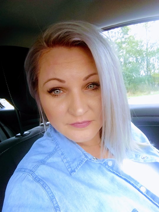 Portret kobiety z platynowymi włosami i niebieską koszulą dżinsową, siedzącej w samochodzie.