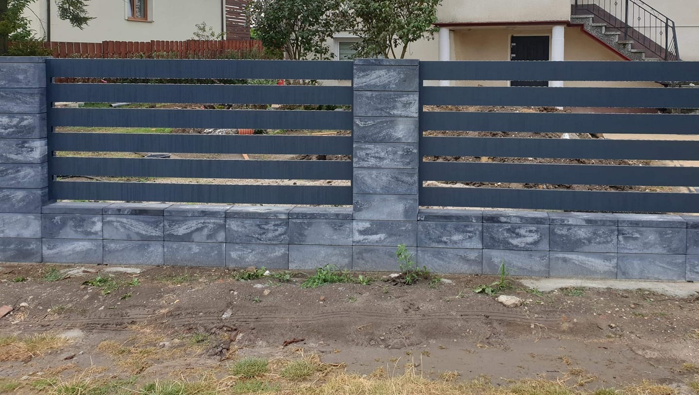 Nowoczesne ogrodzenie z poziomych, szarych paneli i słupków z szarej kostki, widok z poziomu gruntu, w tle dom z metalowymi schodami.