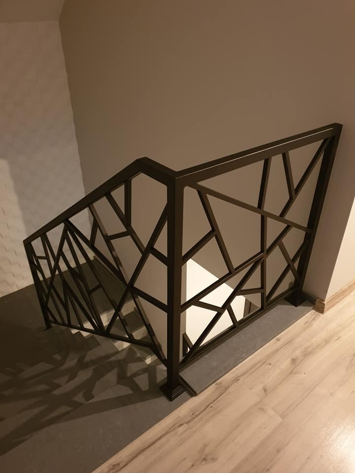 Nowoczesna metalowa balustrada schodowa z geometrycznym wzorem, widok z góry, ciemne wykończenie na tle jasnych ścian i schodów.