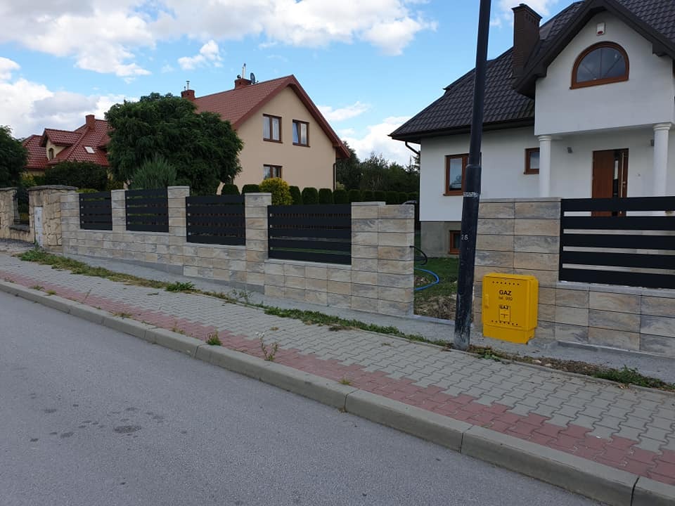 Nowoczesne ogrodzenie z paneli poziomych i słupków z kamienia w Busko-Zdroju, widok z poziomu ulicy, na tle domy jednorodzinne pod błękitnym niebem.