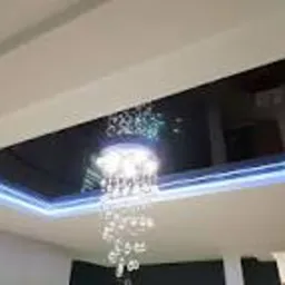 Biały sufit z czarnym, błyszczącym panelem centralnym, podświetlonym niebieskim LED, z kryształowym żyrandolem w centrum.