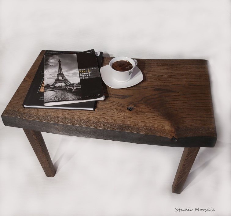 Drewniany stolik śniadaniowy z ciemnymi nogami, na blacie książki z motywem wieży Eiffla i filiżanka kawy na białym tle.