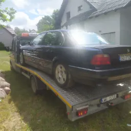 Czarny samochód BMW załadowany na lawetę na tle domu jednorodzinnego i zieleni.