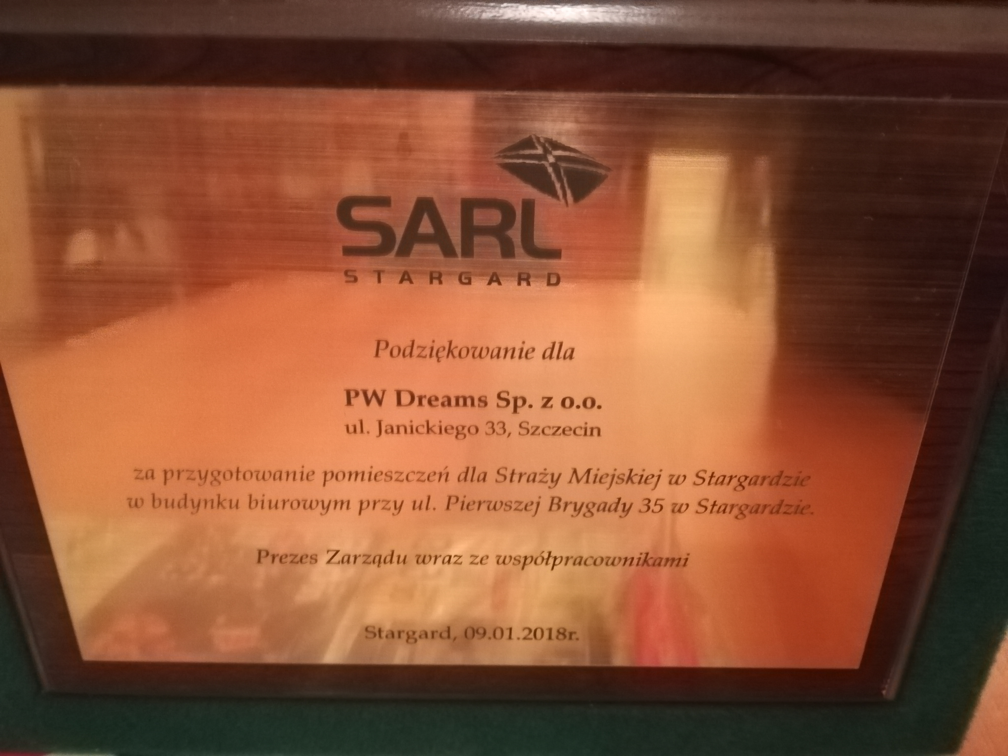 Tablica pamiątkowa z podziękowaniem dla PW Dreams Sp. z o.o. za przygotowanie pomieszczeń dla Straży Miejskiej w Stargardzie, umieszczona w drewnianej ramce.