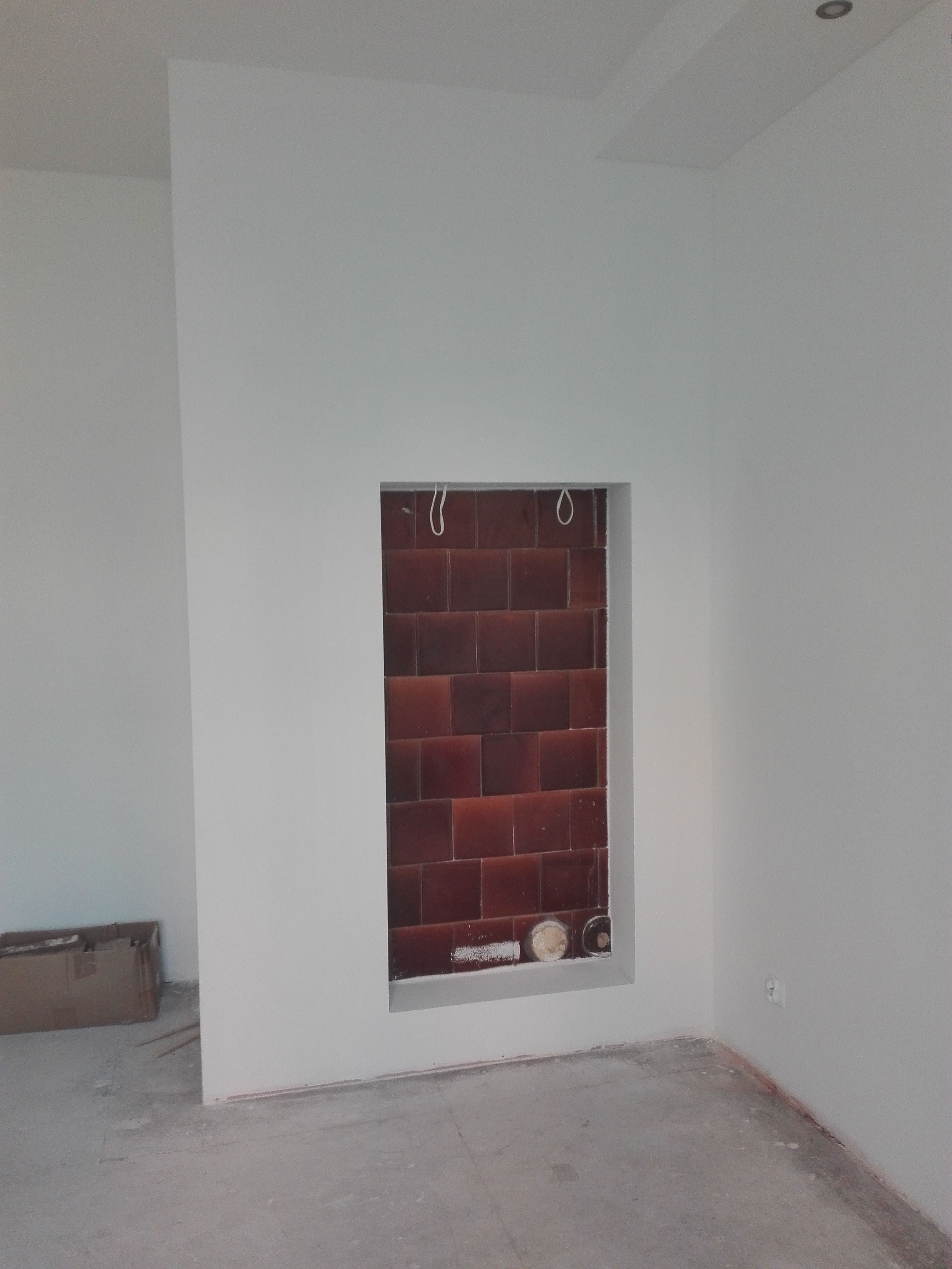 Wnęka z brązowymi płytkami w białej ścianie, widoczne przewody i pozostałości po pracach wykończeniowych.