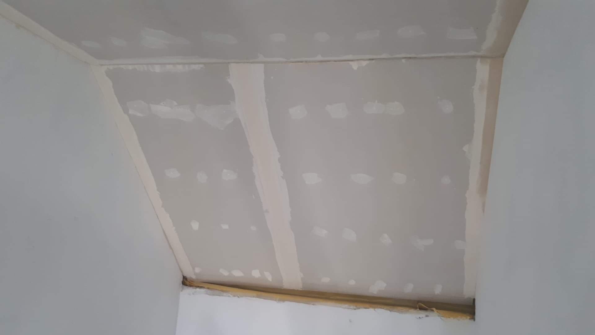 Skośny sufit poddasza w trakcie wykańczania, widoczne łączenia płyt zaszpachlowane, ale przed ostatecznym szlifowaniem, z widocznymi śladami po wkrętach.