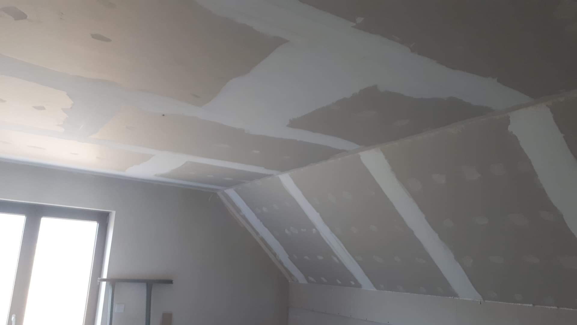 Poddasze w trakcie wykańczania: widoczne łączenia płyt na skosach i suficie, częściowo zaszpachlowane, przygotowane do dalszych prac wykończeniowych.